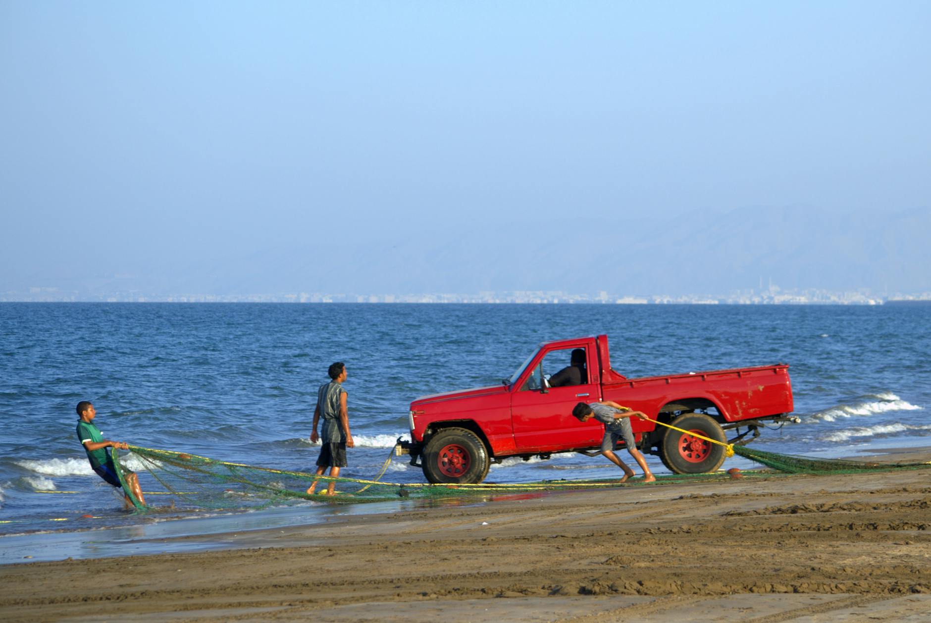 Czerwony pickup Toyota Hilux pomaga rybakom ciągnąć sieci na plaży