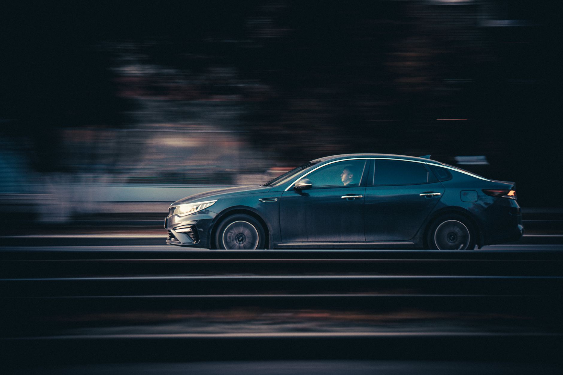 Czarny Mercedes jedzie nocą po drodze, rozmyte światła podkreślają szybkość