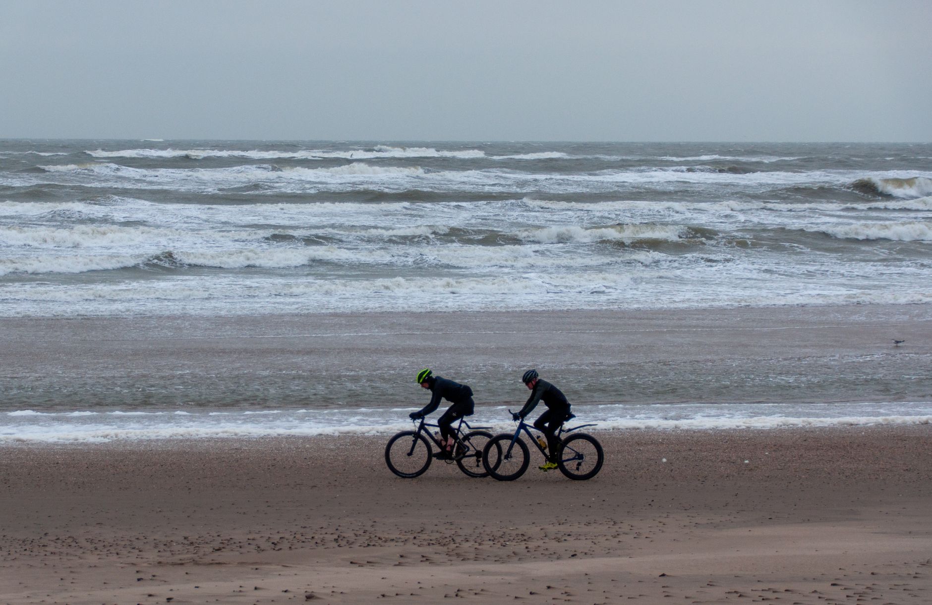 Dwoje rowerzystów jedzie plażą Bałtyku w wietrzny, pochmurny dzień